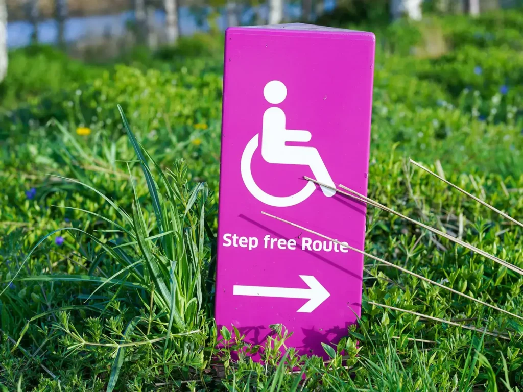 Das Bild zeigt eine Rasenfläche mit einem Hinweisschild für einen stufenfreien Weg für mehr Barrierefreiheit (accessibility)